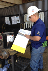 A worker reviews the safety data sheet for required PPE before putting a protective coating on thread connectors for drill pipe at the Quail Tools rental facility in Odessa, Texas. Quail Tools is a subsidiary of Parker Drilling.